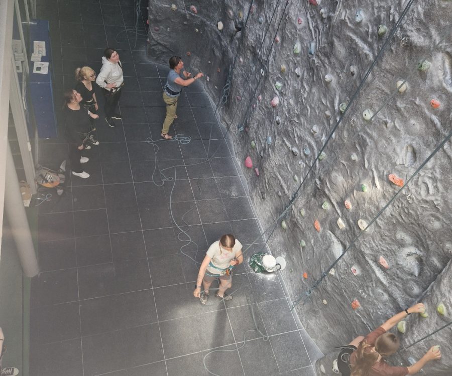 Looking down at the top of a climbing wall, 3 girls wait to climb