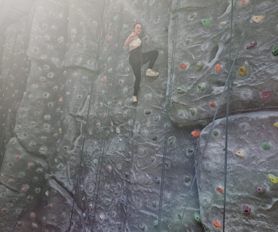 A girl turns to face the camera halfway up a climbing wall