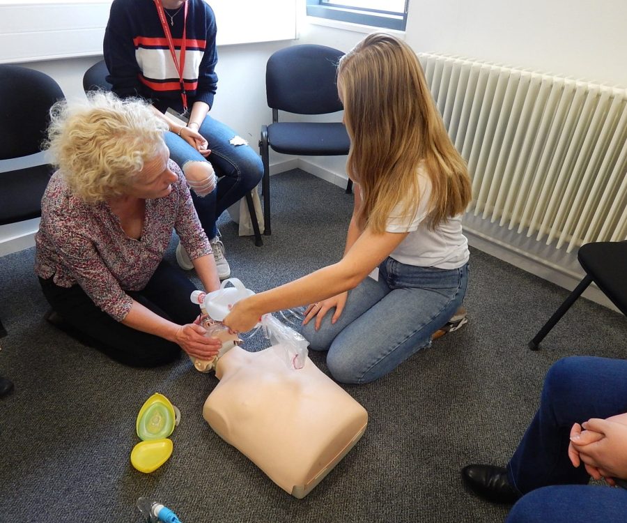 A woman shows a girl how to do CPR on a dummy