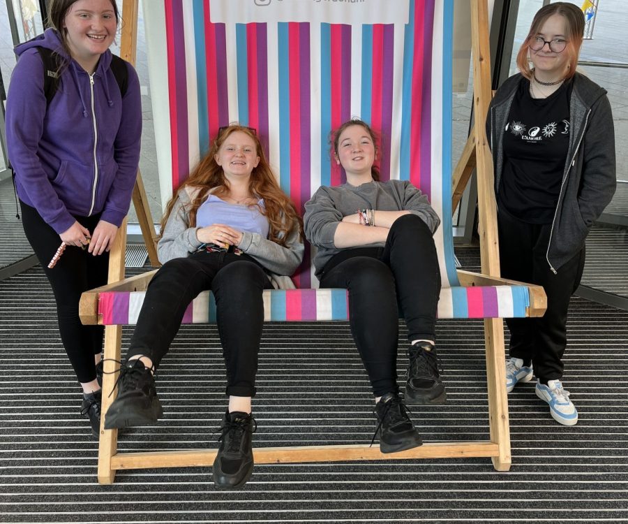 2 girls sit in a giant deck chair while 2 others stand at either side