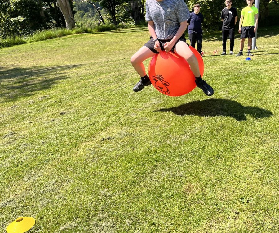 A boy bounces high on a space hopper in a sunny field