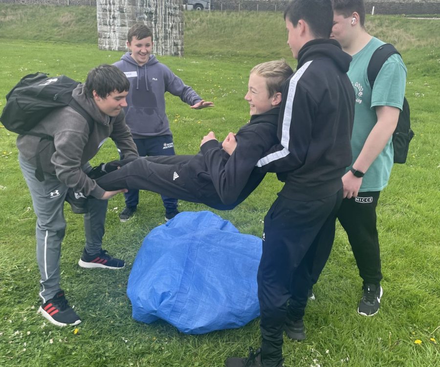 Boys lowering another boy onto a bag full of balloons.