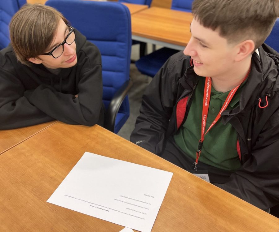 2 boys sit at office chairs having a conversation